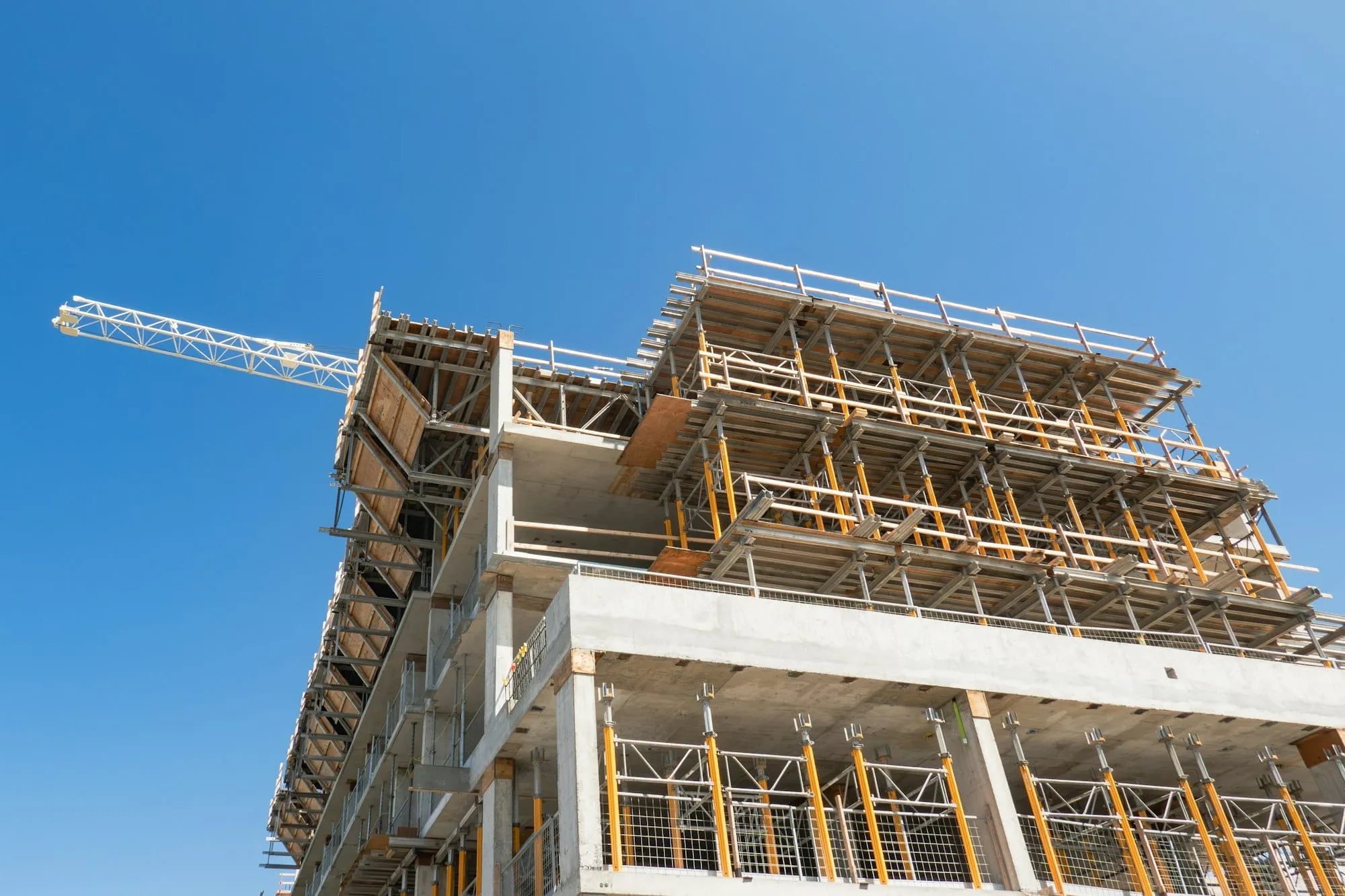 A multi-storey building under construction in a dense city, formwork and reinforcement exposed across several levels.