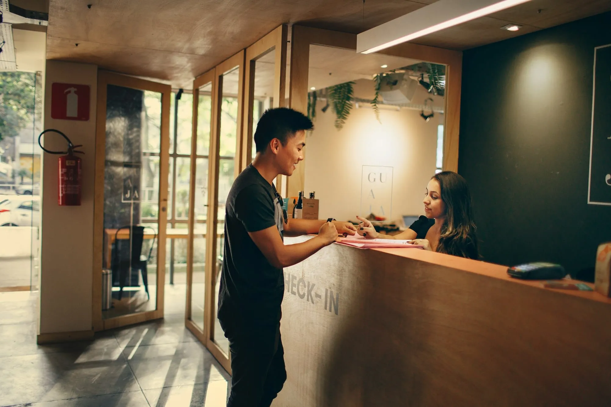 A member of staff at a hotel check-in desk talking with a guest across the counter.